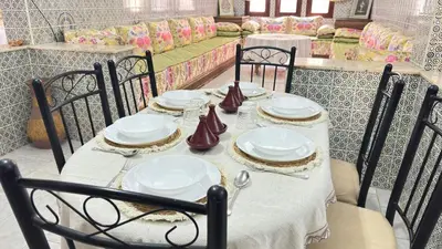 a table with chairs and white plates on it at Appartement style traditionnel climatisé chaufé in Fès