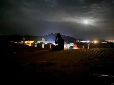 a man sitting on the beach at night at Oasis Merzouga Retreat in Merzouga