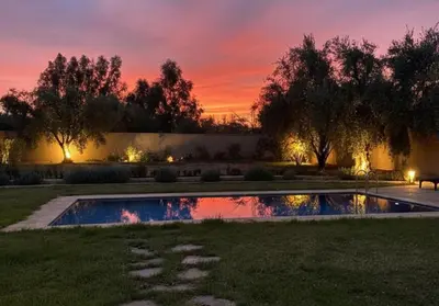 a pool in a yard with a sunset in the background at Oasis de Calme Villa Piscine Hammam & Vues Atlas in Ouled el guerne