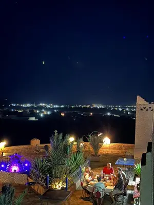 a group of people sitting at tables on a patio at night at Kasbah Hôtel Rama in Merzouga