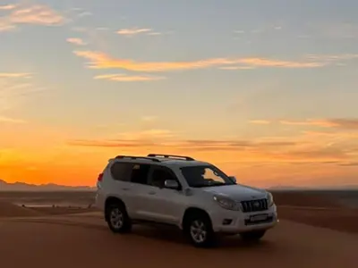 a white suv driving in the desert at sunset at Kasbah Hôtel Rama in Merzouga