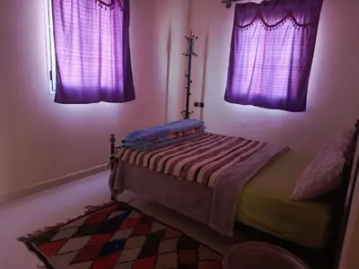 a bedroom with purple curtains and a bed with a rug at Dar Bedda in Merzouga