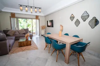 a living room with a wooden table and blue chairs at Appartement de Luxe à Majorelle in Oulad Akkou