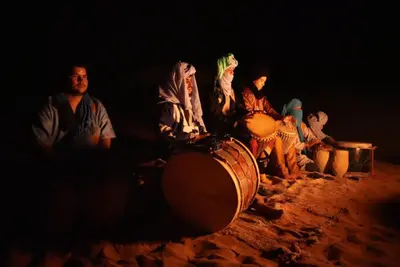 a group of people sitting on a drum in the sand at Merzouga tarwla camp in Merzouga