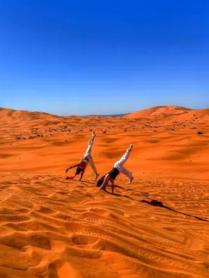 two people are doing yoga in the desert at Merzouga tarwla camp in Merzouga