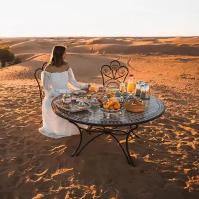 a woman in a wedding dress sitting at a table in the desert at Merzouga Explore Desert Camp in Merzouga