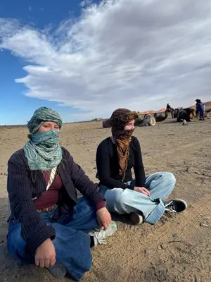 two women sitting on the sand on a beach at Merzouga Infinity Dunes Camp in Merzouga