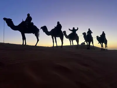 a group of people riding on camels in the desert at Merzouga Infinity Dunes Camp in Merzouga