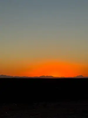 a sunset in the desert with mountains in the background at Merzouga Infinity Dunes Camp in Merzouga