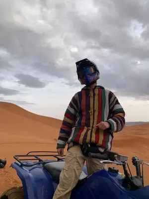 a man standing on a motorcycle in the desert at Nomad Haven Luxury Camp in Merzouga