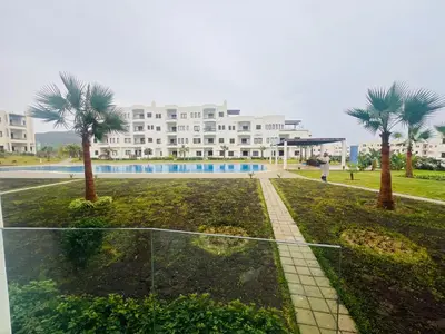 a large white building with palm trees in front of it at Colina Smir par Immo Marina Vacances de Rêve D1-3 in Oulad Akkou