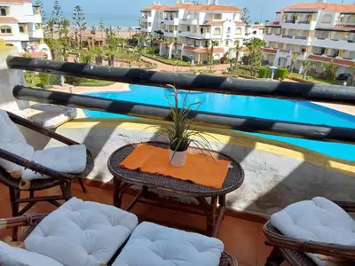 a balcony with a table and chairs and a pool at Appartement front de mer à Sidi Rahal