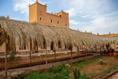 a building with a straw roof with a building in the background at Riad Du Sud in Tamsahelt