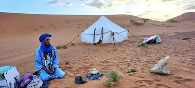 a man sitting in the sand in front of a tent at Isolé Bivouac Merzouga in Merzouga