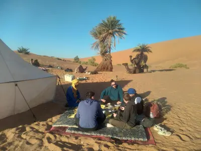 a group of people sitting in front of a tent in the desert at Isolé Bivouac Merzouga in Merzouga