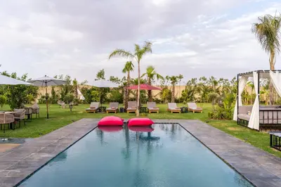 a pool at a resort with tables and umbrellas at Villa Hasard Marrakech in Had Abdallah Rhiat