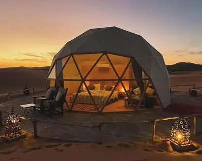 a tent in the desert with a couch and a chair at Erg Chebbi Luxury Geodesic Camp in Merzouga