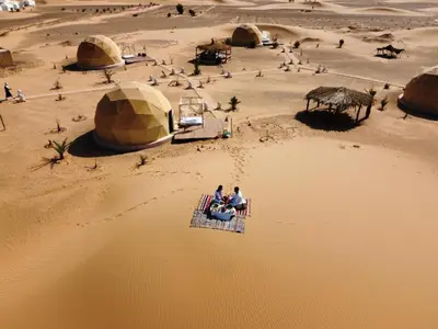 two people sitting on a table in the desert at Erg Chebbi Luxury Geodesic Camp in Merzouga