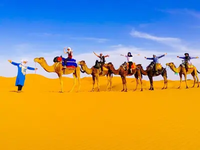 a group of people riding on camels in the desert at Golden Silence Camp in Merzouga