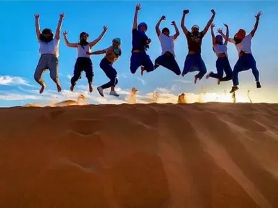 a group of people jumping in the air in the desert at Golden Silence Camp in Merzouga
