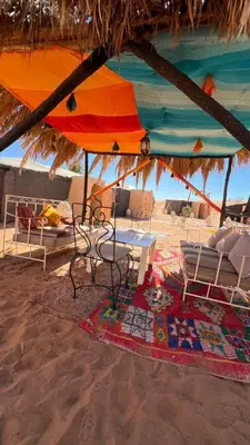 a table and chairs under an umbrella on the beach at Golden Silence Camp in Merzouga