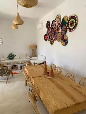 a living room with a wooden table and plates on the wall at Maison El Alia in Merzouga