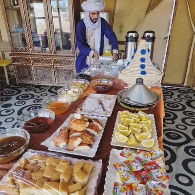 a man standing in front of a table with food at Merzouga Desert Night Luxury Camp Tours & Cozy Rooms in Rissani