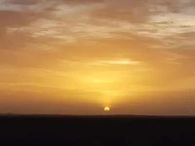 a sunset with the sun in the sky at StarlitDesertCamp in El Gouera