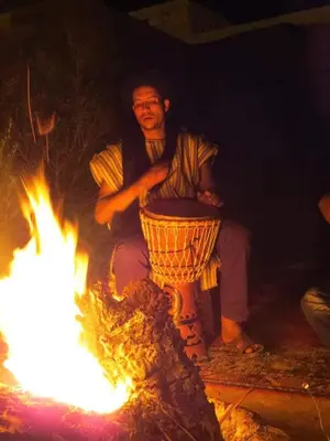 a man sitting next to a fire with a pot at Bivouac Dune Iriki in Foum Zguid