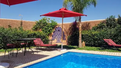 a pool with a table and a red umbrella at Authentic Riad with swimming pool and private garden