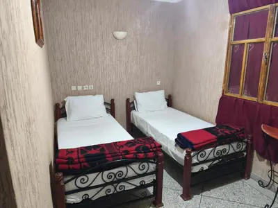 two beds in a small room with a window at Hotel El Golla in Er Rachidia