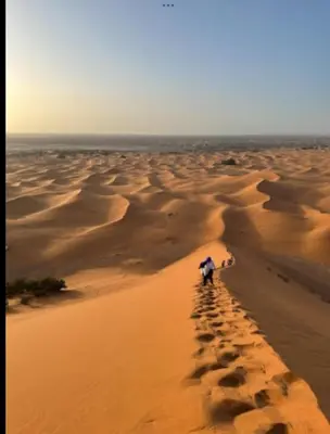 a person walking in the desert with an umbrella at Merzouga Outdoors Private Nomad Expedition in Merzouga