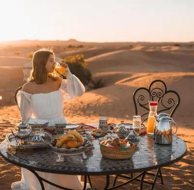 a woman sitting at a table in the desert at Merzouga Luxury Camp in Merzouga