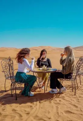 three women sitting at a table in the desert at Merzouga Luxury Camp in Merzouga