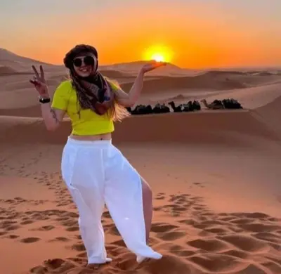 a woman standing in the desert with the sunset in the background at Merzouga Luxury Camp in Merzouga