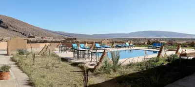 a swimming pool with tables and chairs and mountains in the background at Kasbah Tissint in Tissint