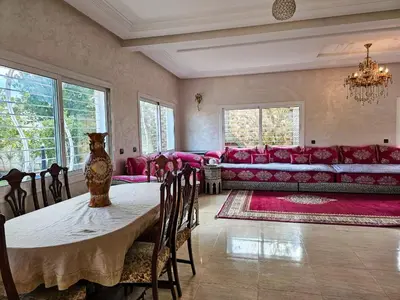 a living room with a table and a red couch at Villa rue imouzzer in Fès
