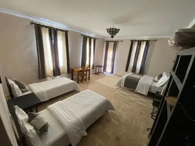 a bedroom with two beds and a table and windows at Itrane sahara Auberge in Taouz