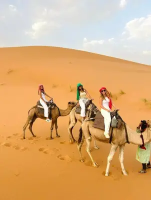 three women riding on camels in the desert at Star Desert Camp Merzouga in Merzouga