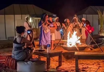 a group of people standing around a fire at Top Desert Camp in Merzouga
