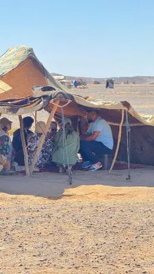 a group of people sitting under a tent in the desert at Desert Halo Camp in Merzouga