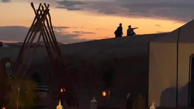 two people standing on top of a hill at sunset at Desert Halo Camp in Merzouga