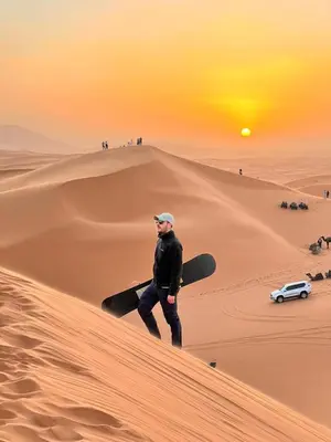 a man walking on a sand dune with a snowboard at merzouga best luxury camp in Merzouga