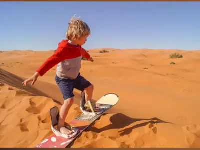 a young boy standing on a surfboard in the desert at merzouga best luxury camp in Merzouga