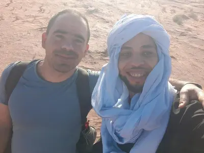 a man with a blue hijab sitting next to another man at M'hamid El Ghizlane, Provinz Zagora in Oulad Akkou