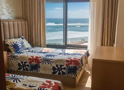 a bedroom with two beds and a view of the beach at Appartement avec vue panoramique sur la mer, climatisation, terrasse & ascenseur in Oulad Akkou
