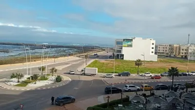 a street with cars parked on a road next to the ocean at Appartement avec vue panoramique sur la mer, climatisation, terrasse & ascenseur in Oulad Akkou