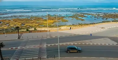 a car driving down a road next to the ocean at Appartement avec vue panoramique sur la mer, climatisation, terrasse & ascenseur in Oulad Akkou