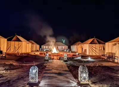 a group of huts at night with smoke at Infinite Sky Luxury Camp Merzouga in Merzouga