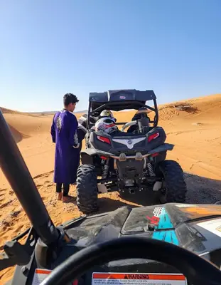 a man standing next to a wheeler in the desert at Infinite Sky Luxury Camp Merzouga in Merzouga